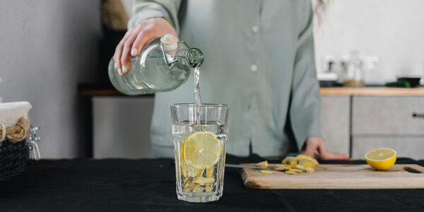 žena sipa vodu s limunom u visoku čašu, svetlo iz prozora