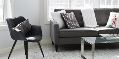 sivi kauč, stakleni sto i tekstilni tepih pored prozora