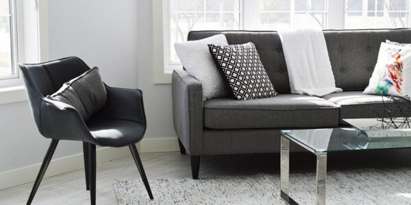 sivi kauč, stakleni sto i tekstilni tepih pored prozora