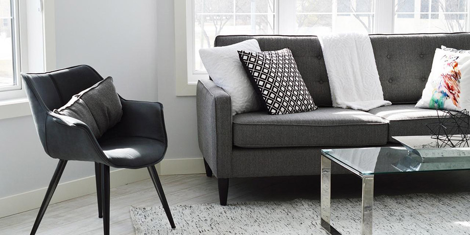 sivi kauč, stakleni sto i tekstilni tepih pored prozora