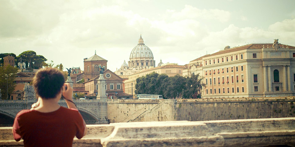 Osoba stoji s leđa i fotografiše gradski pejzaž sa velikom kupolom u pozadini