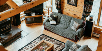 Drveni dnevni boravak sa sofama prekrivenim pokrivačima, staklenim stolićem i kamenom peći