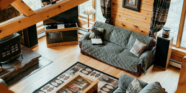 Drveni dnevni boravak sa sofama prekrivenim pokrivačima, staklenim stolićem i kamenom peći