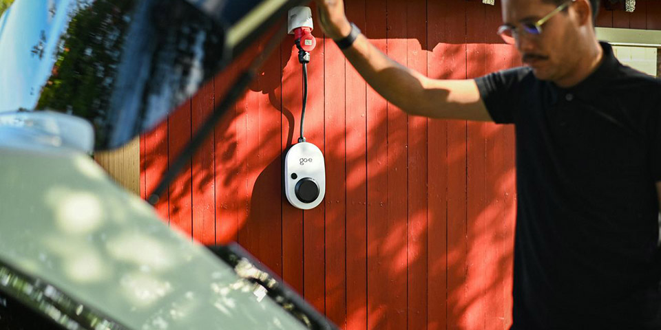 Beli zidni punjač i kabl za električni automobil na crvenom drvenom zidu