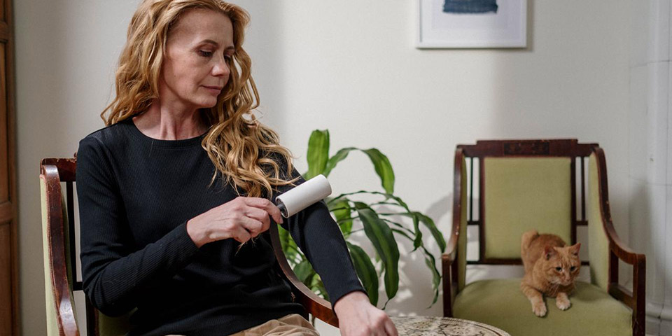 Žena koristi rolicu za uklanjanje dlaka sa rukava dok sedi na stolici