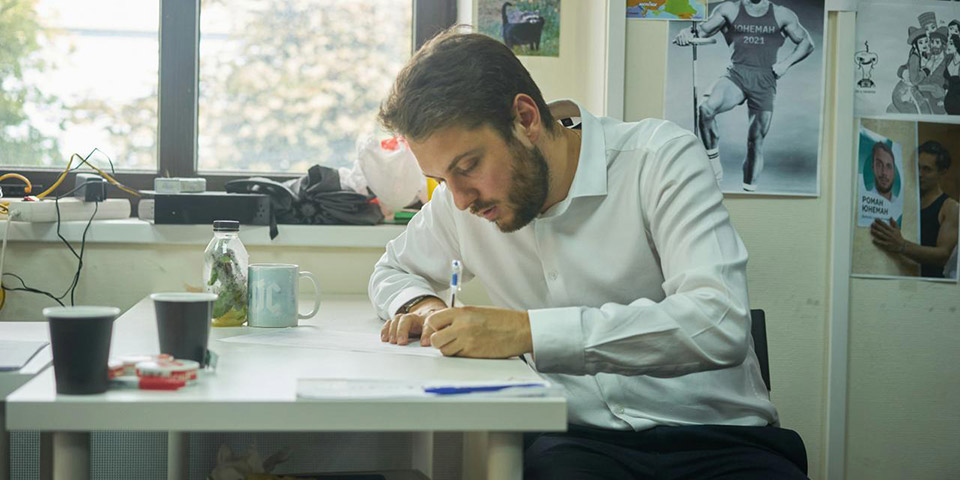 Muškarac u beloj košulji sedi za stolom i piše
